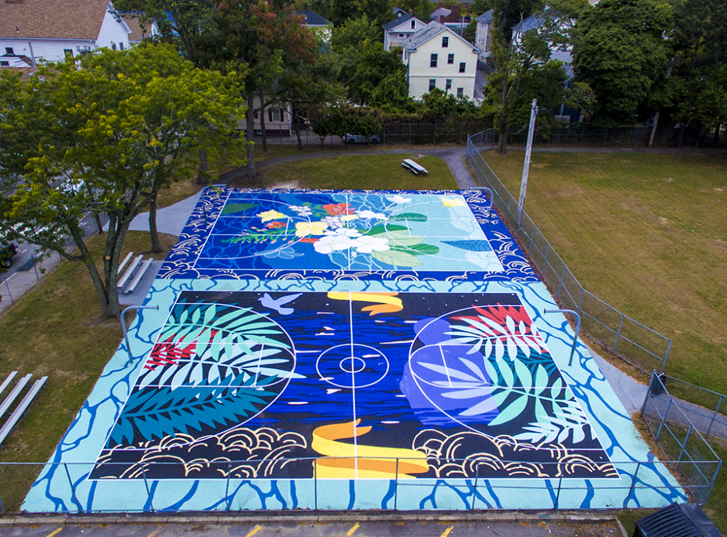 Basketball court in an urban park. Painted mostly in blues and greens, the two sides of the court are complementary, with flowers at one end and non-flowering plants at the other.