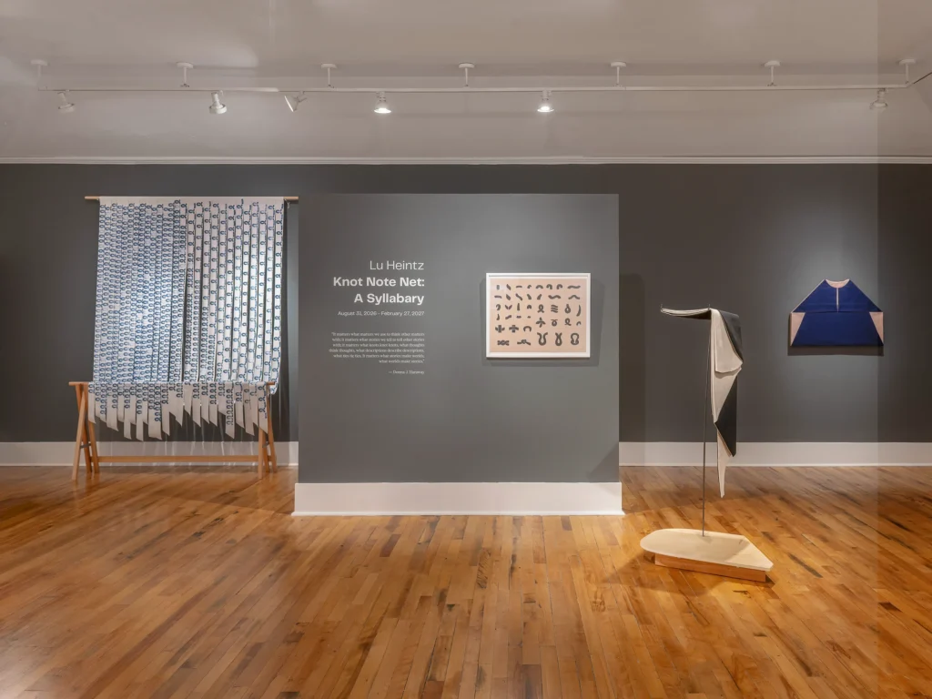 A gallery space with wooden floors, dark gray walls, and four exhibit pieces.