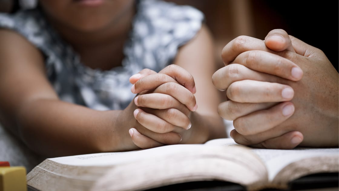 Mother and little girl hands folded in prayer on a Holy Bible together for faith concept in vintage color tone