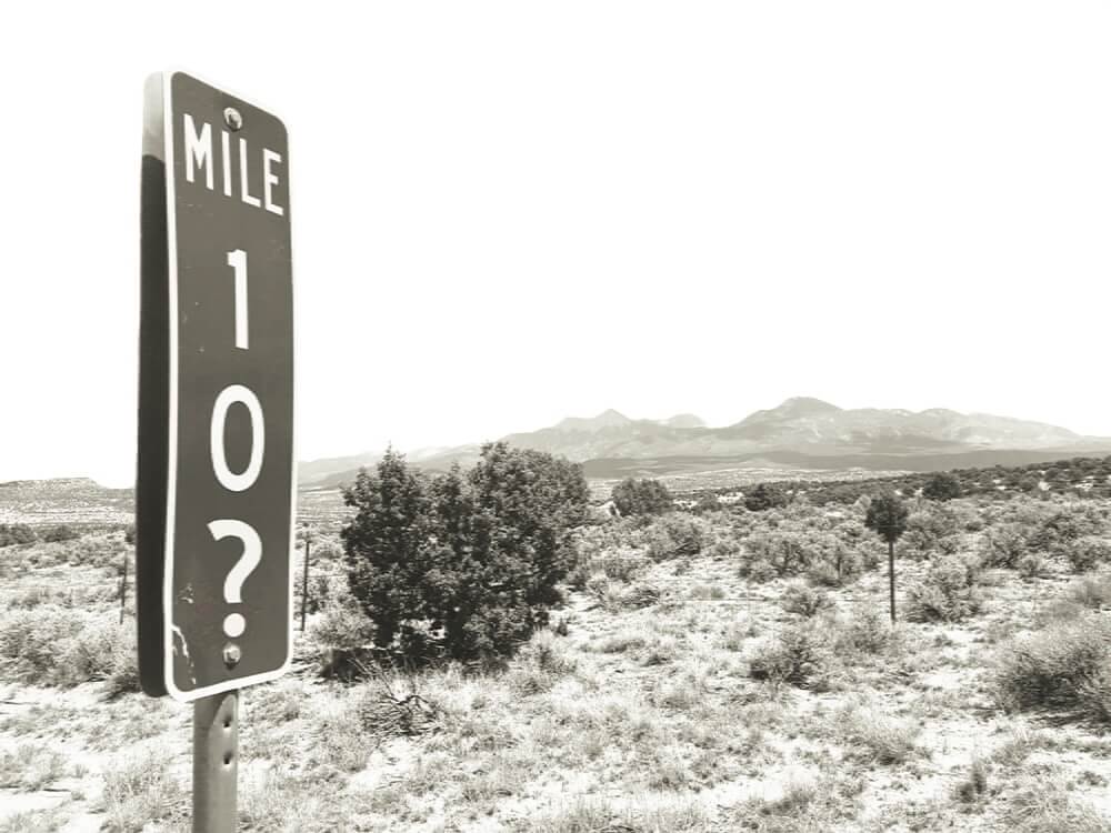 A mile marker that reads 10? in the middle of a desert