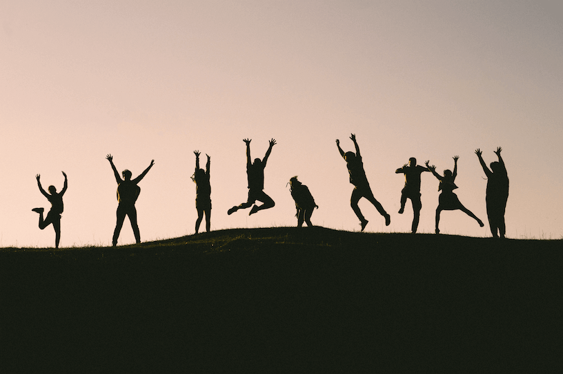 Group of people raising their arms up and jumping on top of a hill.