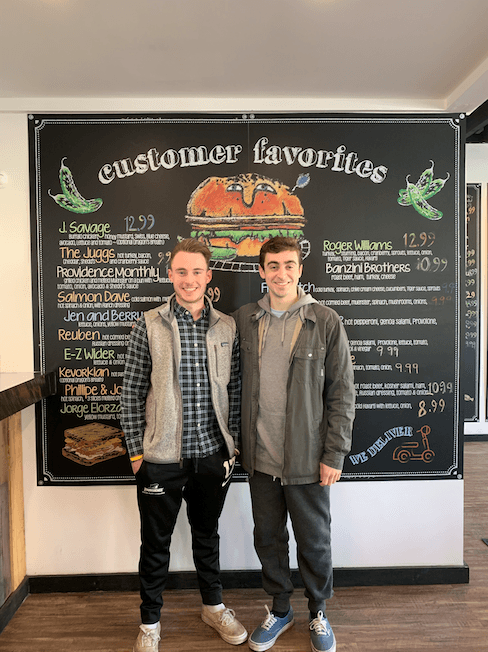 Two students standing in front of a deli menu.