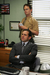 Michael Scott and Dwight Schrute listen to another co-worker in Michael's office.