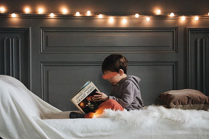 A little boy sitting on a bed reading a book
