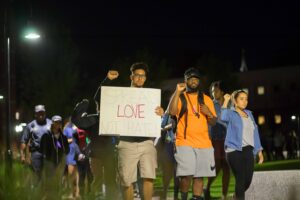 PC students walk in solidarity around campus holding signs that say "spread love not hate."
