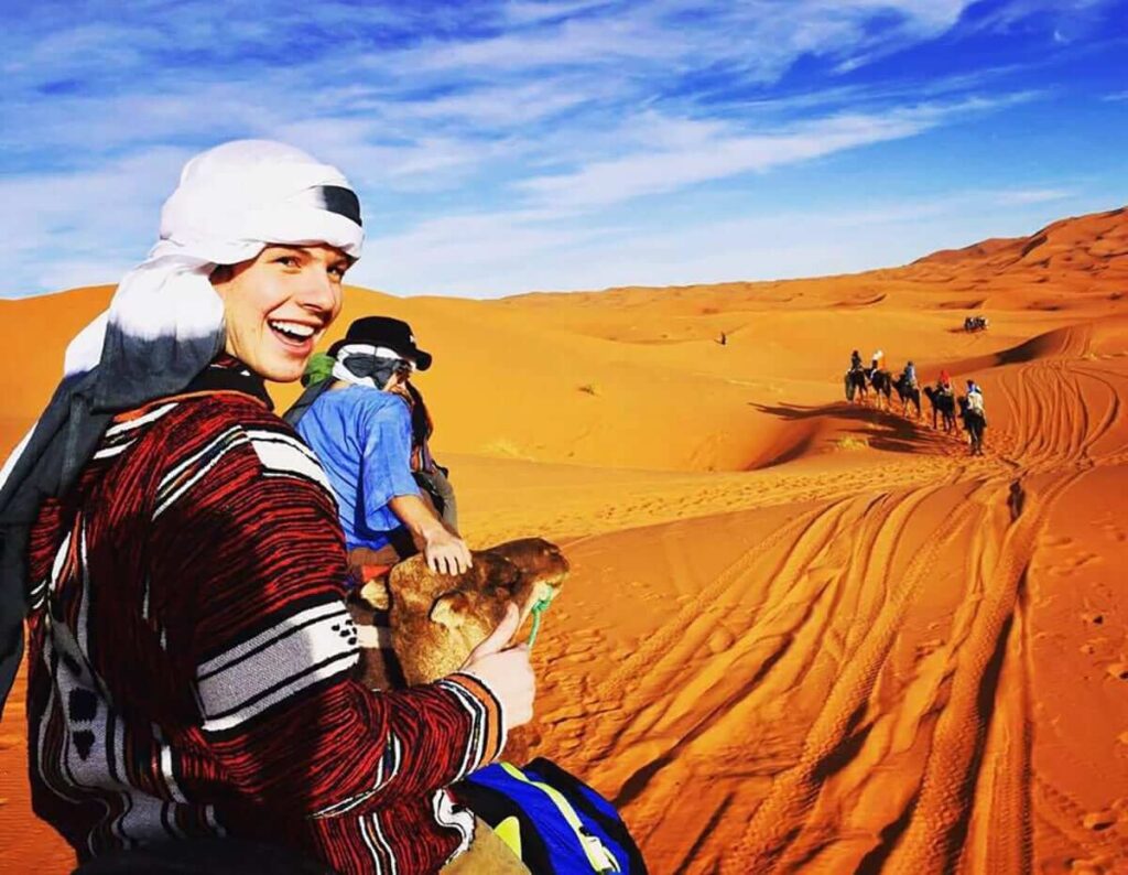 Student rides camel through the desert.
